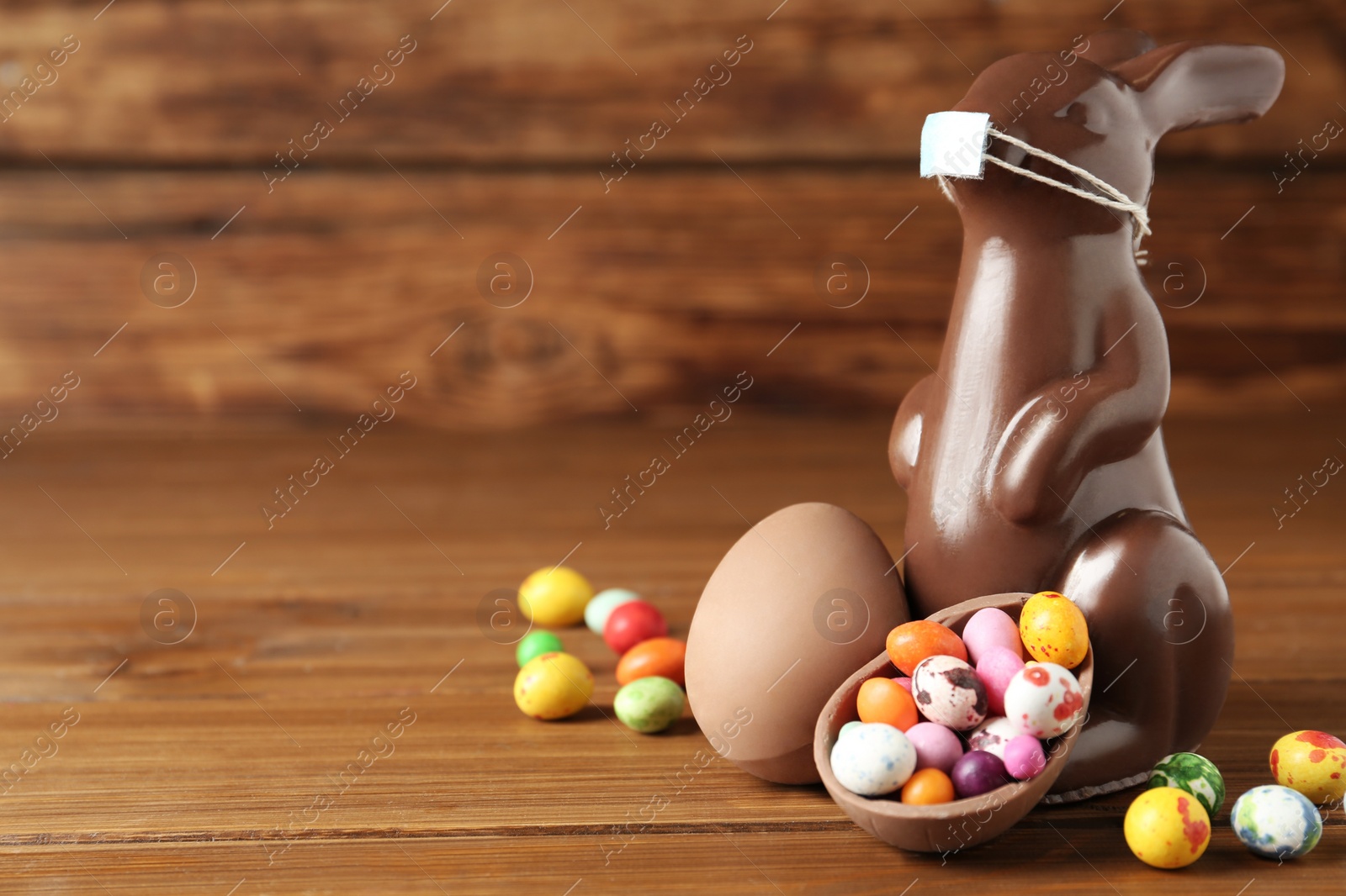 Photo of Chocolate bunny with protective mask, egg shaped candies and space for text on wooden table. Easter holiday during COVID-19 quarantine