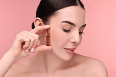 Beautiful young woman holding skincare ampoule on pink background