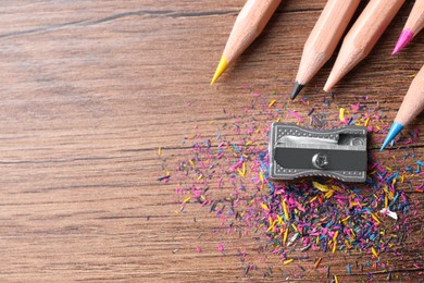 Metal sharpener, colorful graphite crumbs and pencils on wooden table, flat lay. Space for text