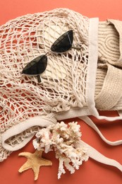 Photo of String bag, sunglasses, slippers, starfish and coral on color background, top view