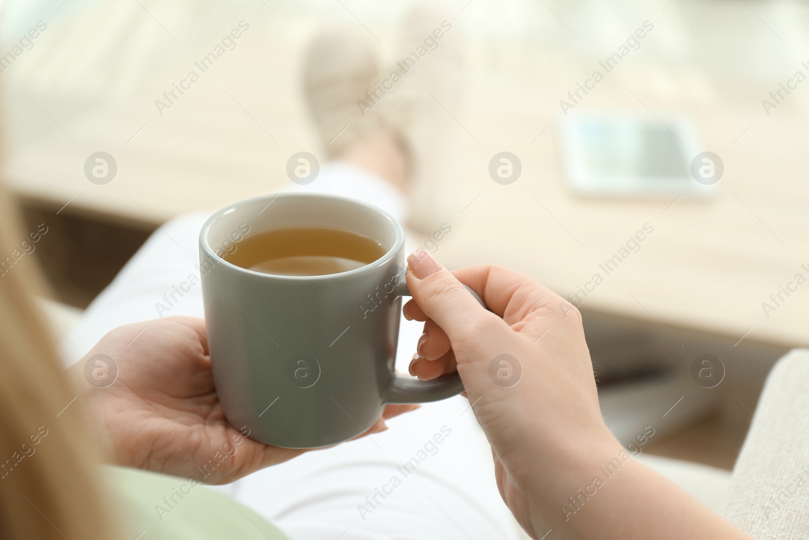 Photo of Young woman with cup of hot tea relaxing at home, closeup