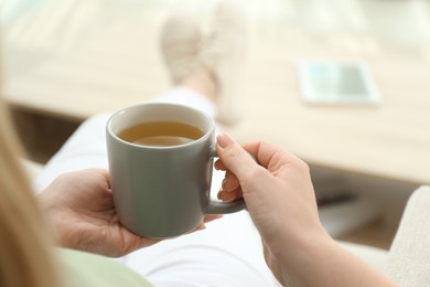 Young woman with cup of hot tea relaxing at home, closeup