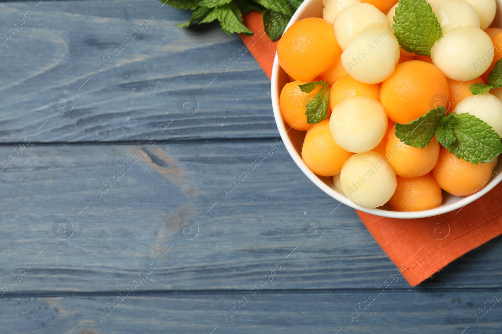 Photo of Melon balls and mint in bowl on blue wooden table, top view. Space for text