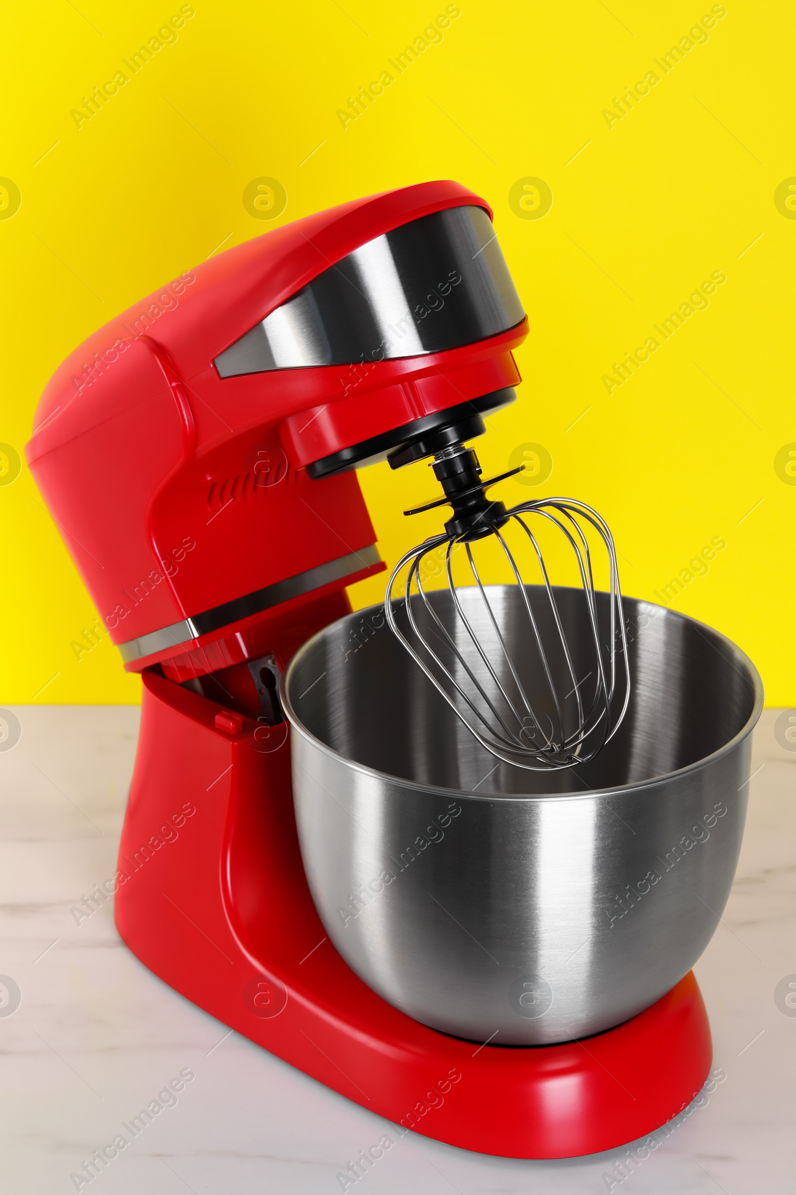 Photo of Modern red stand mixer on white wooden table against yellow background