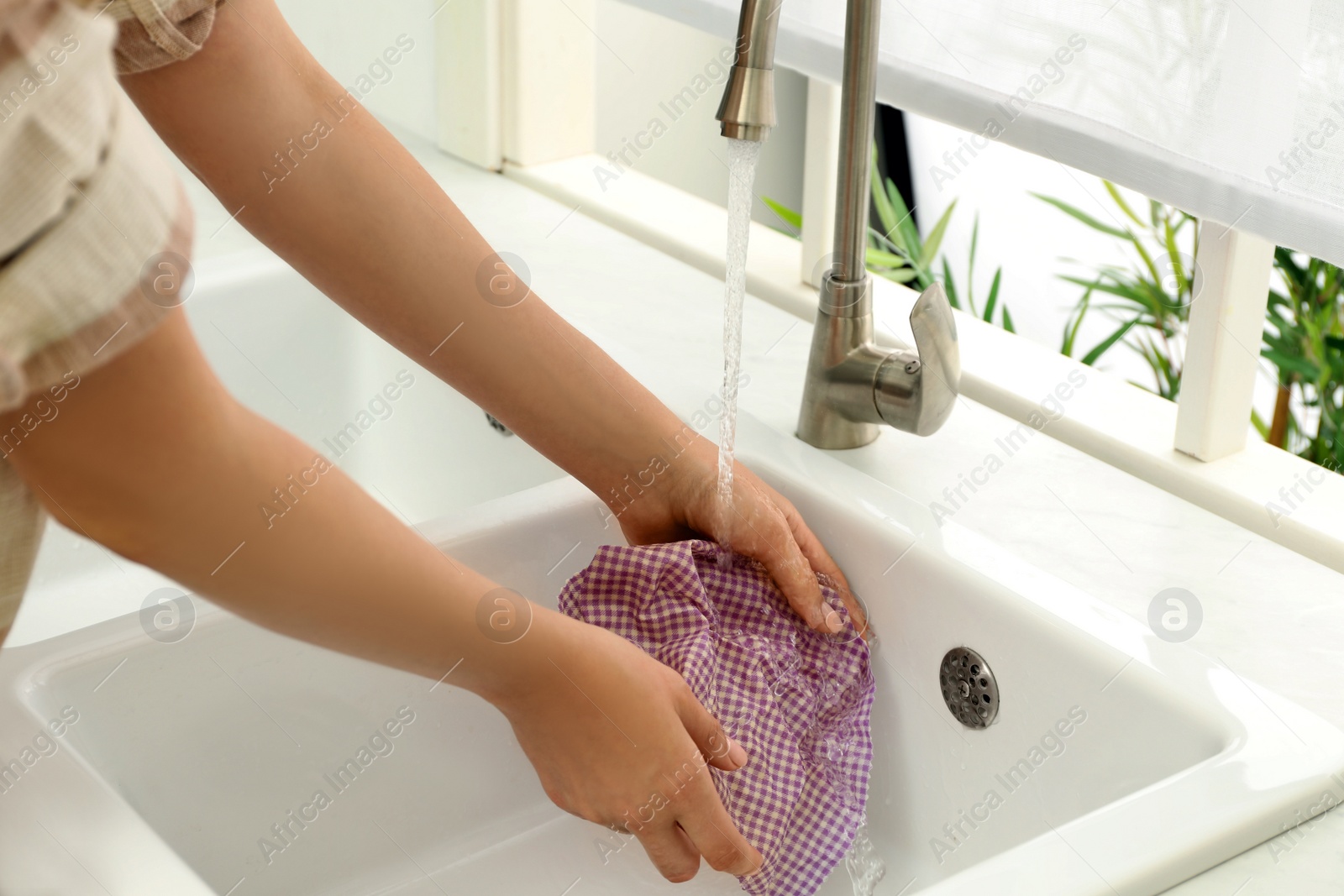 Photo of Woman washing beeswax food wrap under tap water in kitchen sink, closeup