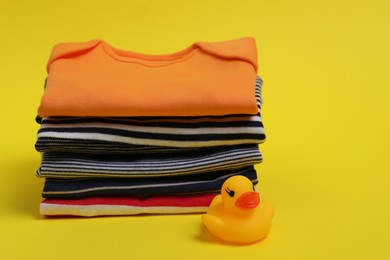 Photo of Stack of clean baby clothes and rubber duck on yellow background