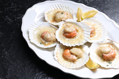 Fried scallops in shells and lemon on black textured table, closeup