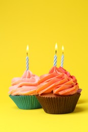 Delicious birthday cupcakes with bright cream on yellow background