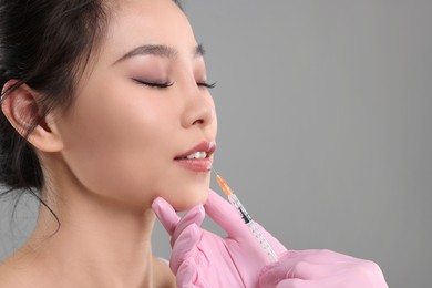 Photo of Woman getting lip injection on grey background