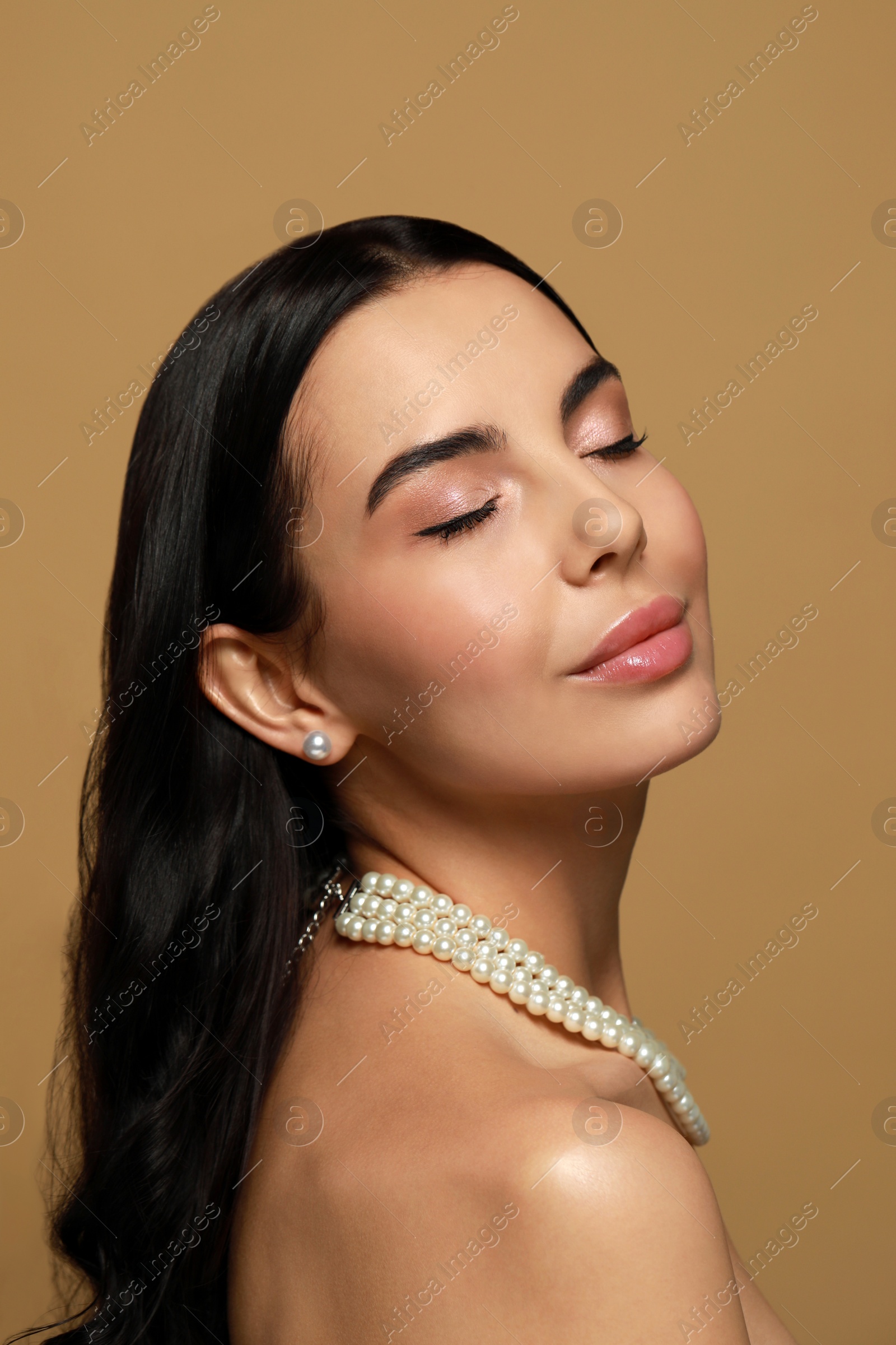 Photo of Young woman wearing elegant pearl jewelry on brown background