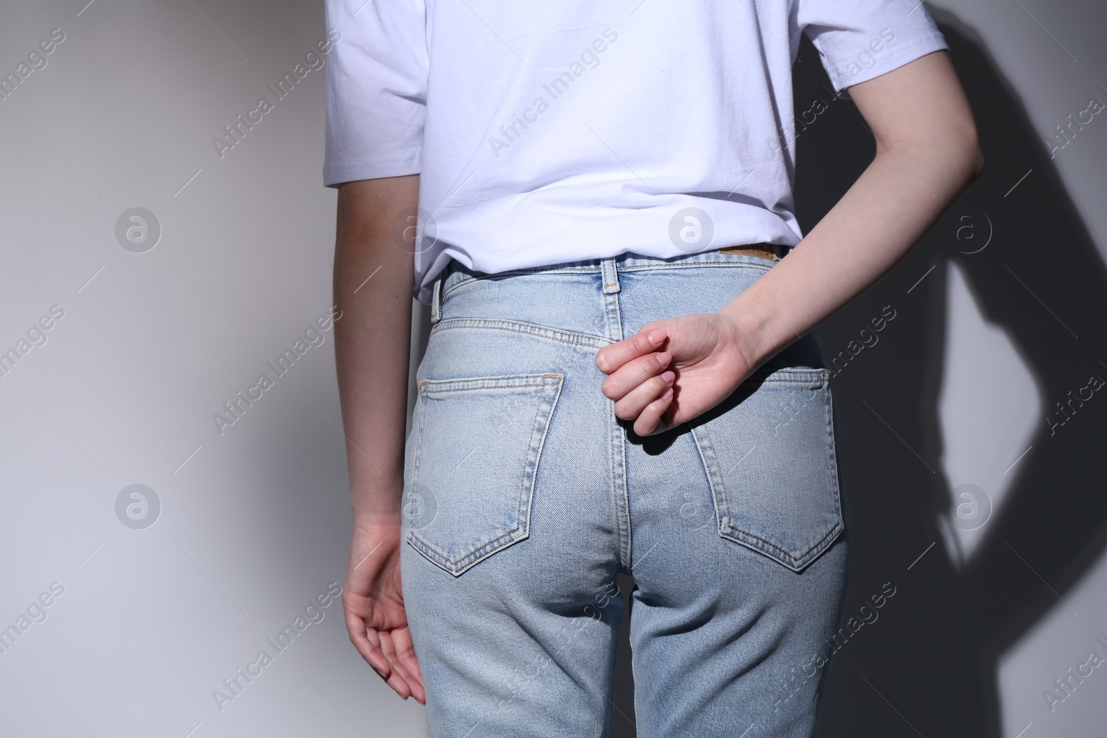 Photo of SOS gesture. Woman showing signal for help behind her back on grey background, back view