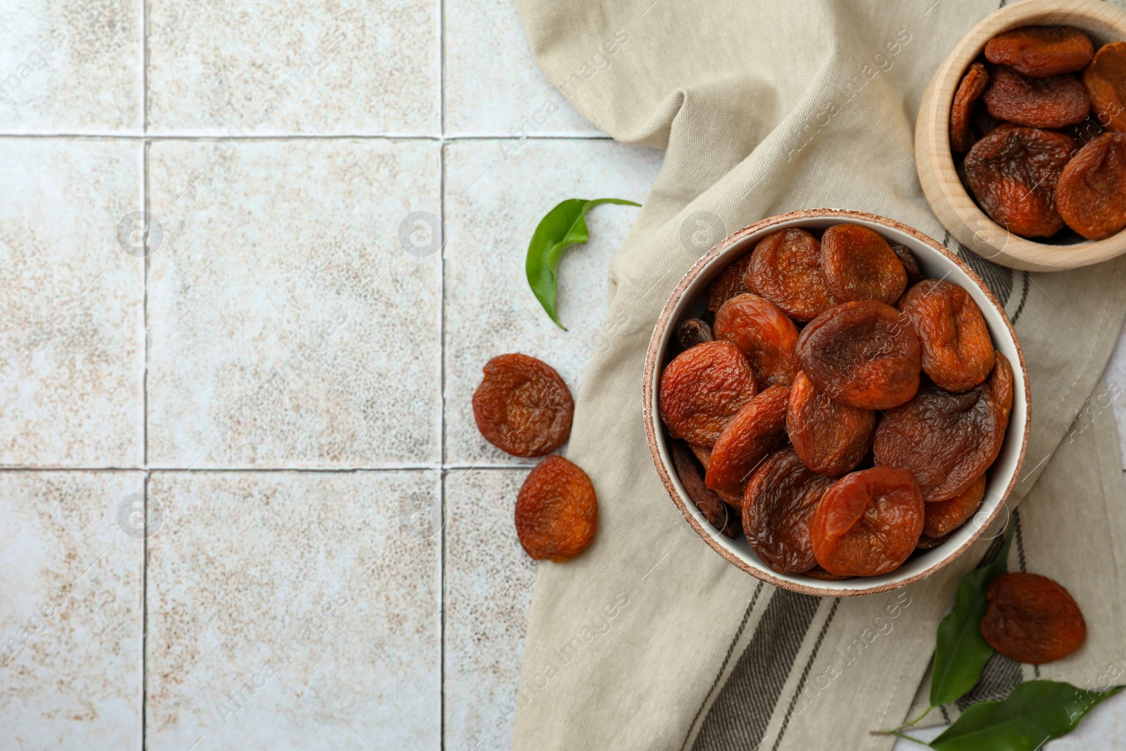 Photo of Tasty apricots, green leaves and space for text on white tiled table, flat lay. Dried fruits