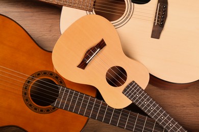 Photo of Ukulele and acoustic guitars on wooden background, flat lay. String musical instruments