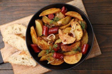 Photo of Delicious baked potato with thin dry smoked sausages in bowl and bread on wooden table, top view