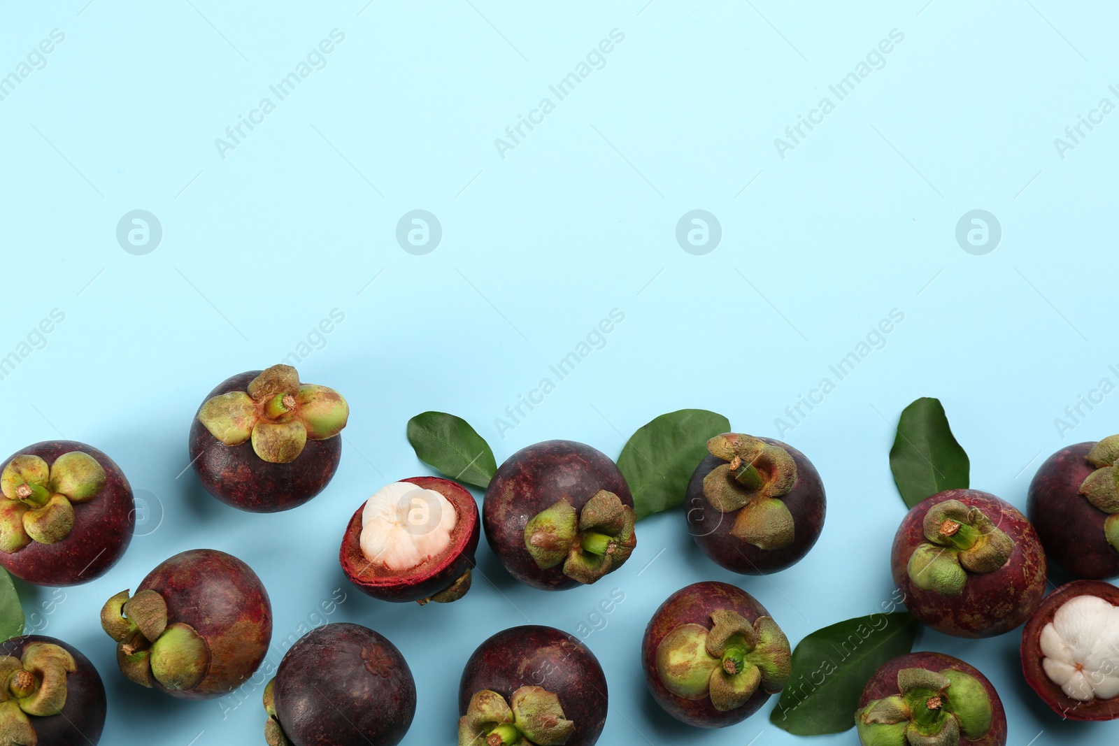 Photo of Fresh ripe mangosteen fruits with green leaves on light blue background, flat lay. Space for text