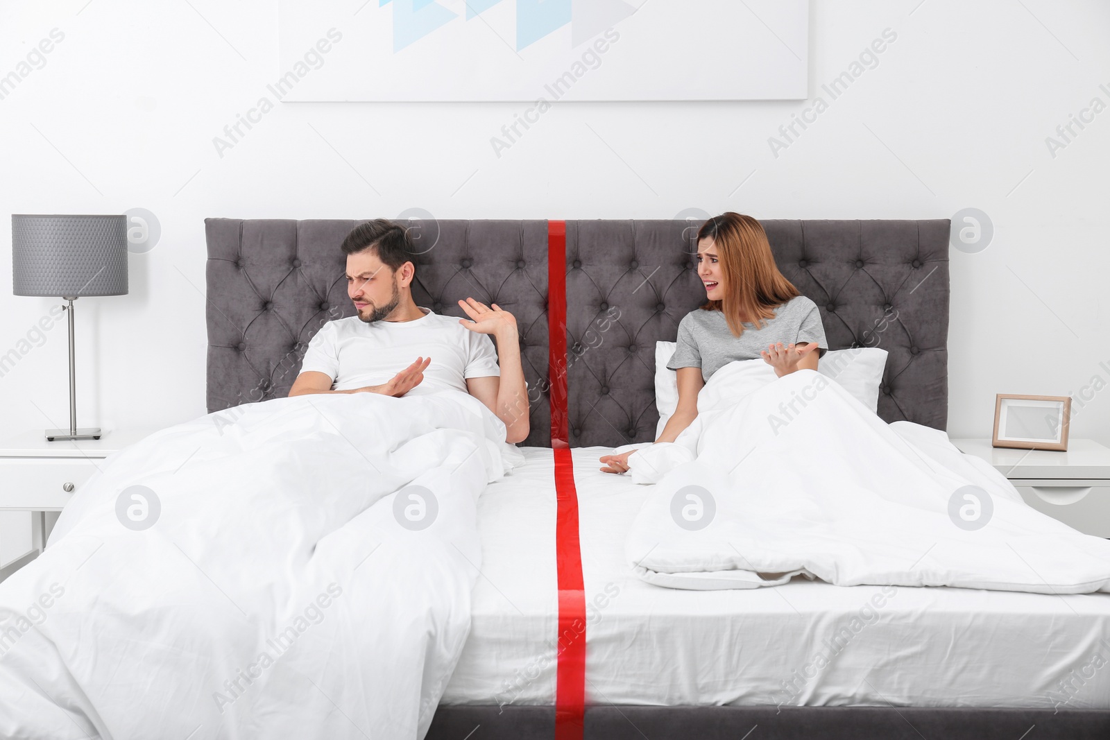 Photo of Couple with relationship problems arguing while lying separately in bed at home