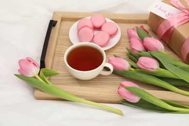 Photo of Tasty breakfast served in bed. Delicious macarons, tea, flowers, gift box and card with phrase I Love You on tray