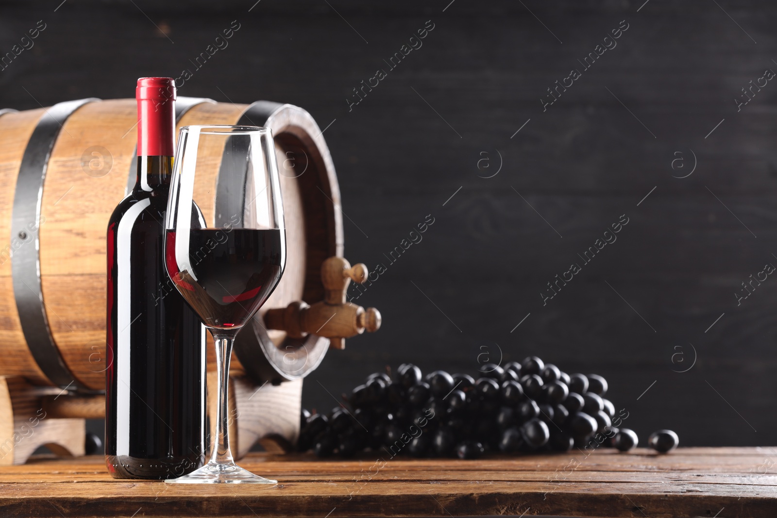 Photo of Delicious wine, wooden barrel and ripe grapes on table. Space for text