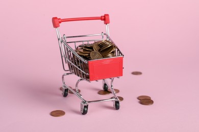 Photo of Small metal shopping cart with coins on pink background