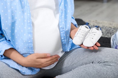 Photo of Pregnant woman holding baby shoes at home, closeup