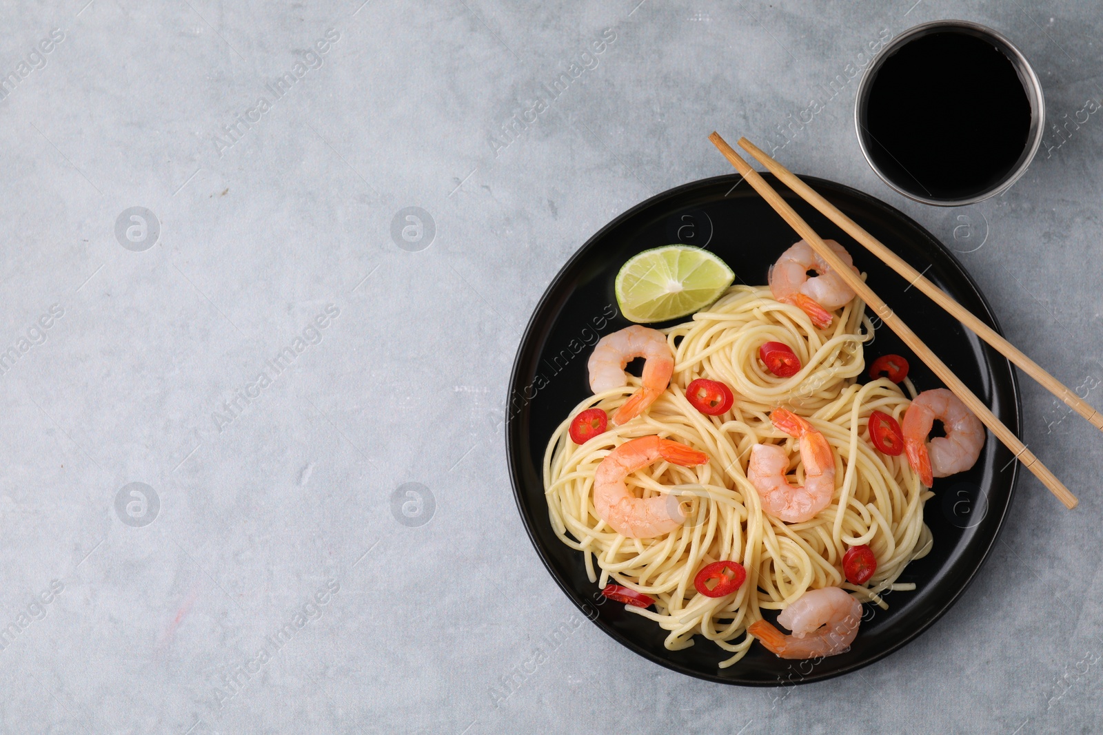 Photo of Tasty spaghetti with shrimps, chili pepper, lime and soy sauce on grey table, flat lay. Space for text