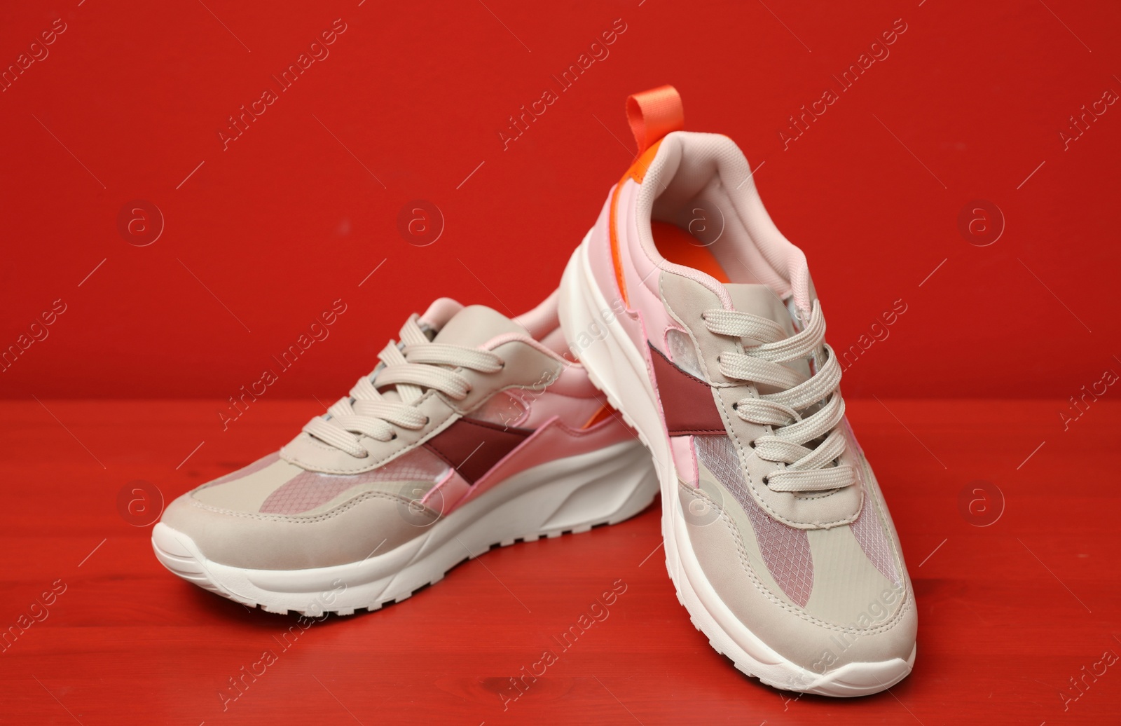 Photo of Stylish women's sneakers on wooden table near red wall