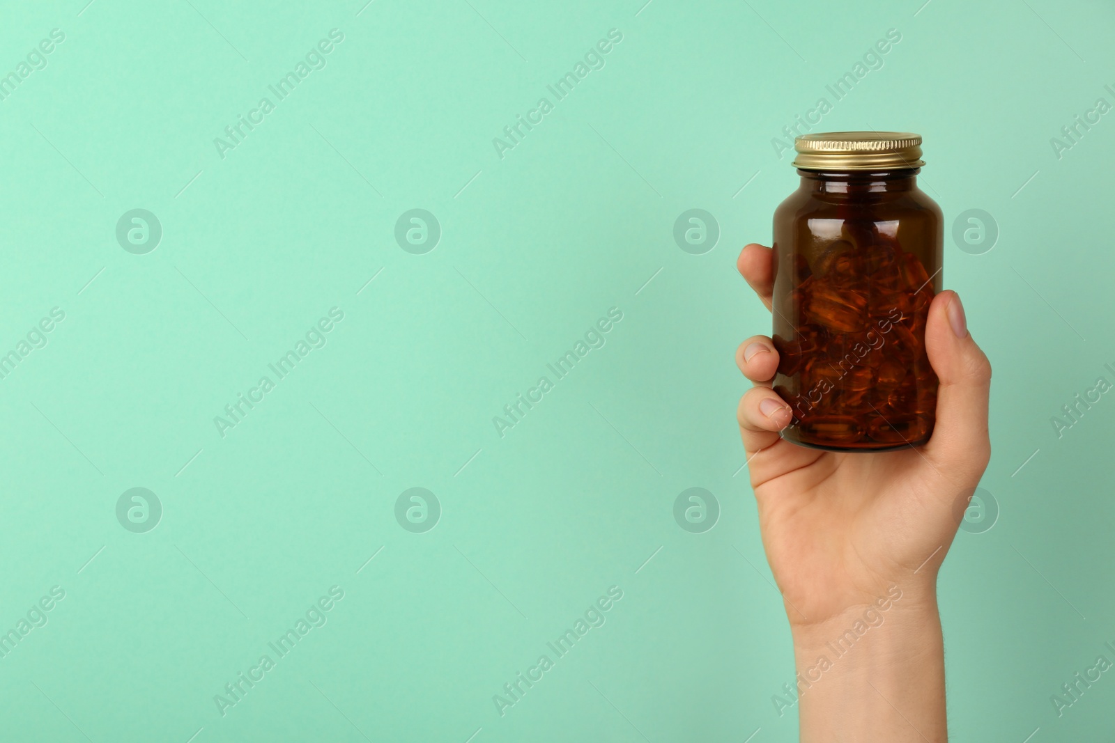 Photo of Woman holding jar with vitamin capsules on turquoise background, closeup. Space for text