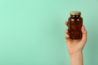 Photo of Woman holding jar with vitamin capsules on turquoise background, closeup. Space for text