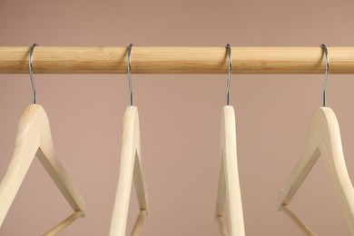 Photo of Empty clothes hangers on wooden rack against light brown background, closeup