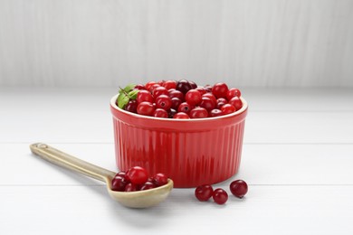 Photo of Fresh ripe cranberries in bowl and spoon on white wooden table, closeup