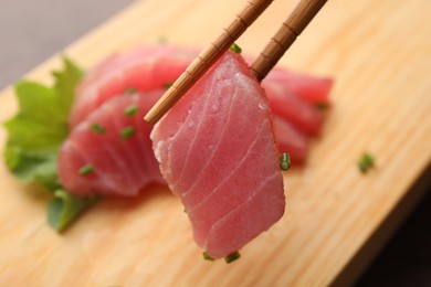 Photo of Holding tasty sashimi (piece of fresh raw tuna) with chopsticks against blurred background, closeup