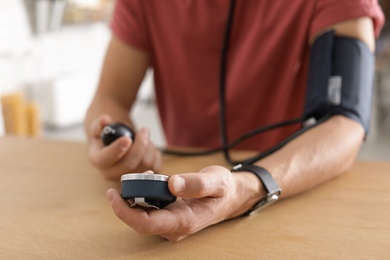 Photo of Man checking blood pressure with sphygmomanometer at table indoors, closeup. Cardiology concept