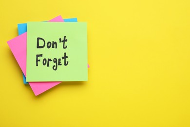 Photo of Paper note with phrase Don' t Forget on yellow background, flat lay. Space for text