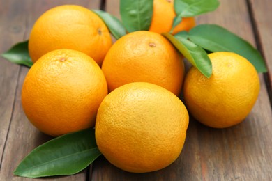 Photo of Many ripe oranges and green leaves on wooden table, closeup