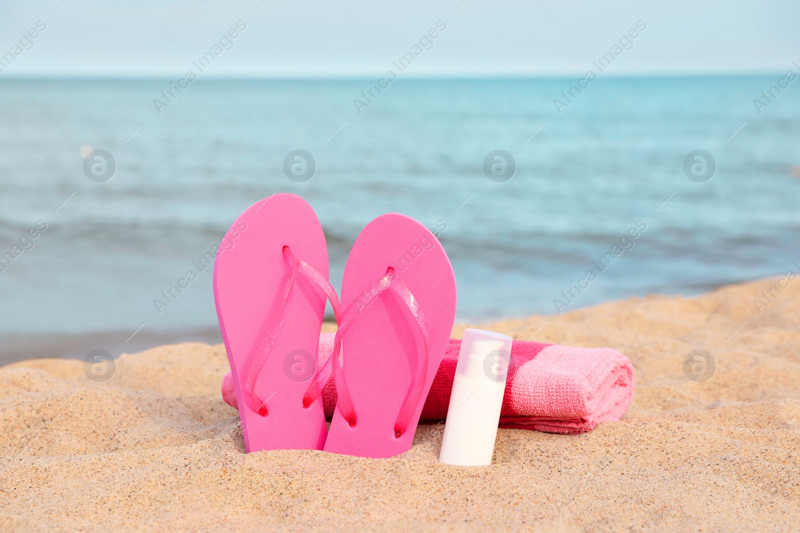 Photo of Beach towel, slippers and sunscreen on sand near sea