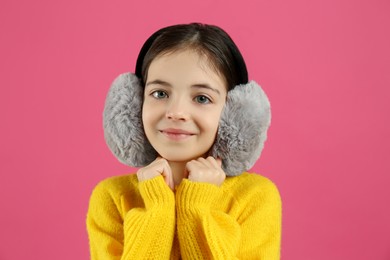 Photo of Cute little girl wearing stylish earmuffs on pink background