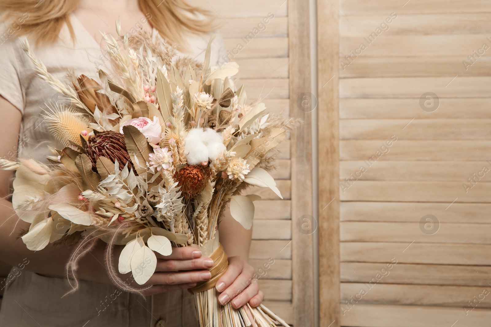 Photo of Woman holding beautiful dried flower bouquet on wooden background, closeup. Space for text