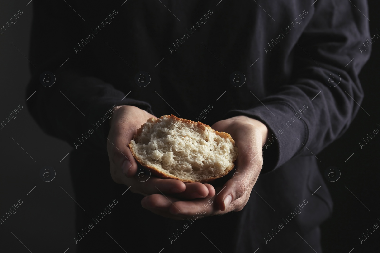 Photo of Poor woman holding piece of bread on dark background, closeup