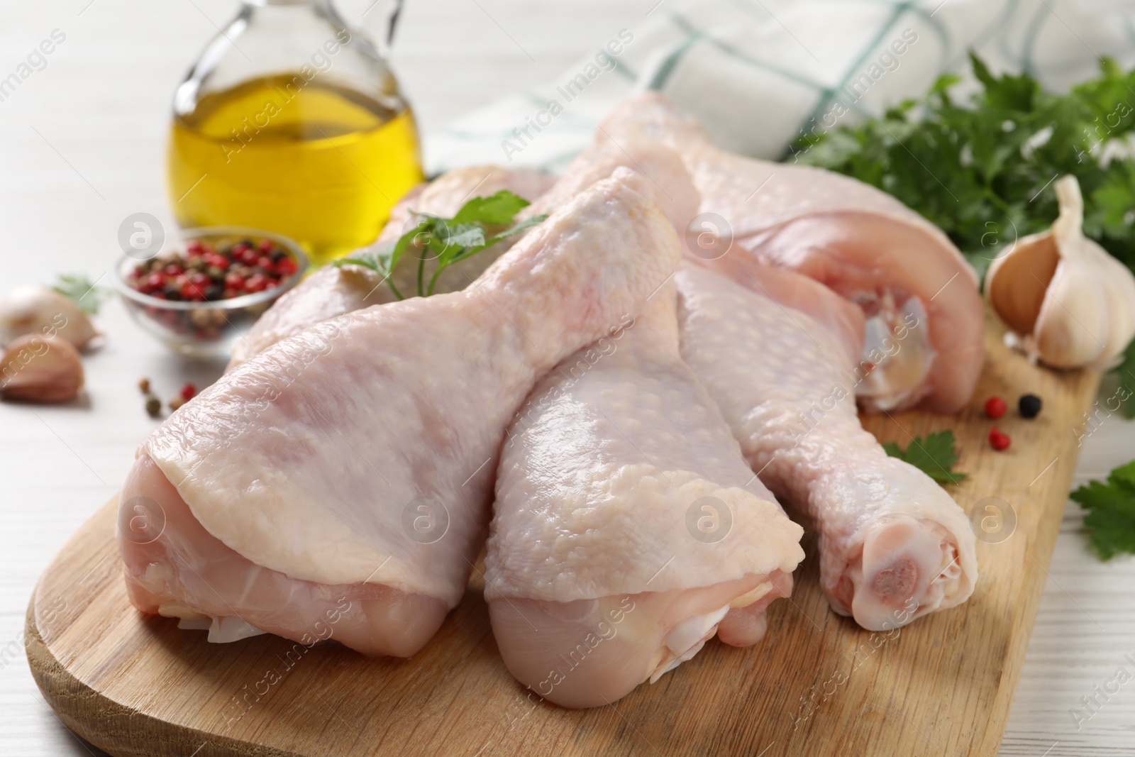 Photo of Raw chicken drumsticks and ingredients on white wooden table, closeup
