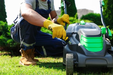 Photo of Young man with screwdriver fixing lawn mower in garden, closeup