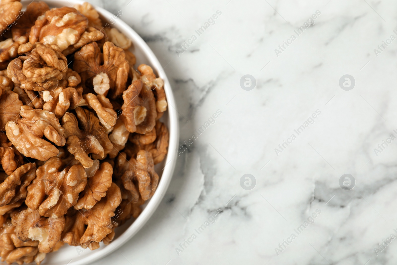 Photo of Plate with walnuts on marble background, top view. Space for text