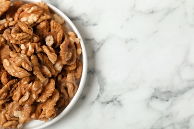 Plate with walnuts on marble background, top view. Space for text