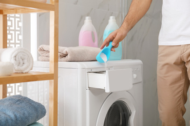 Photo of Man pouring laundry detergent into washing machine drawer in bathroom, closeup