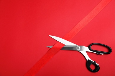 Photo of Stylish scissors and red ribbon on color background, flat lay with space for text. Ceremonial tape cutting