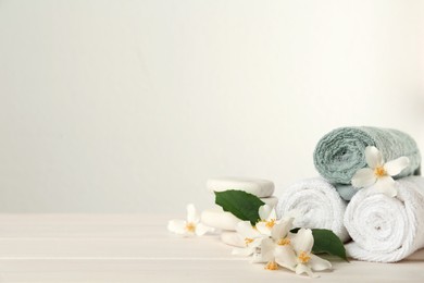 Photo of Beautiful jasmine flowers, spa stones and towels on white wooden table, space for text