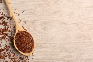 Spoon with dry rooibos leaves on wooden table, flat lay. Space for text