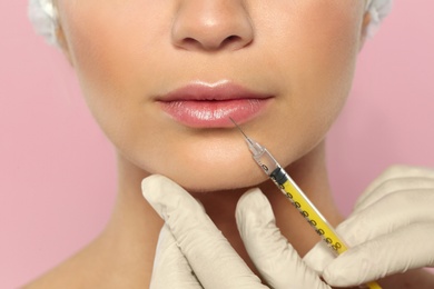 Young woman getting lips injection on color background, closeup. Cosmetic surgery