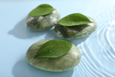 Photo of Spa stones and green leaves on light blue background, closeup