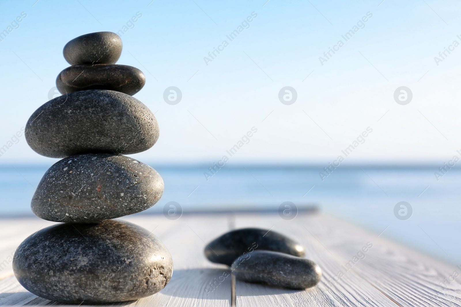 Photo of Stack of dark stones on wooden deck near sea, space for text. Zen concept