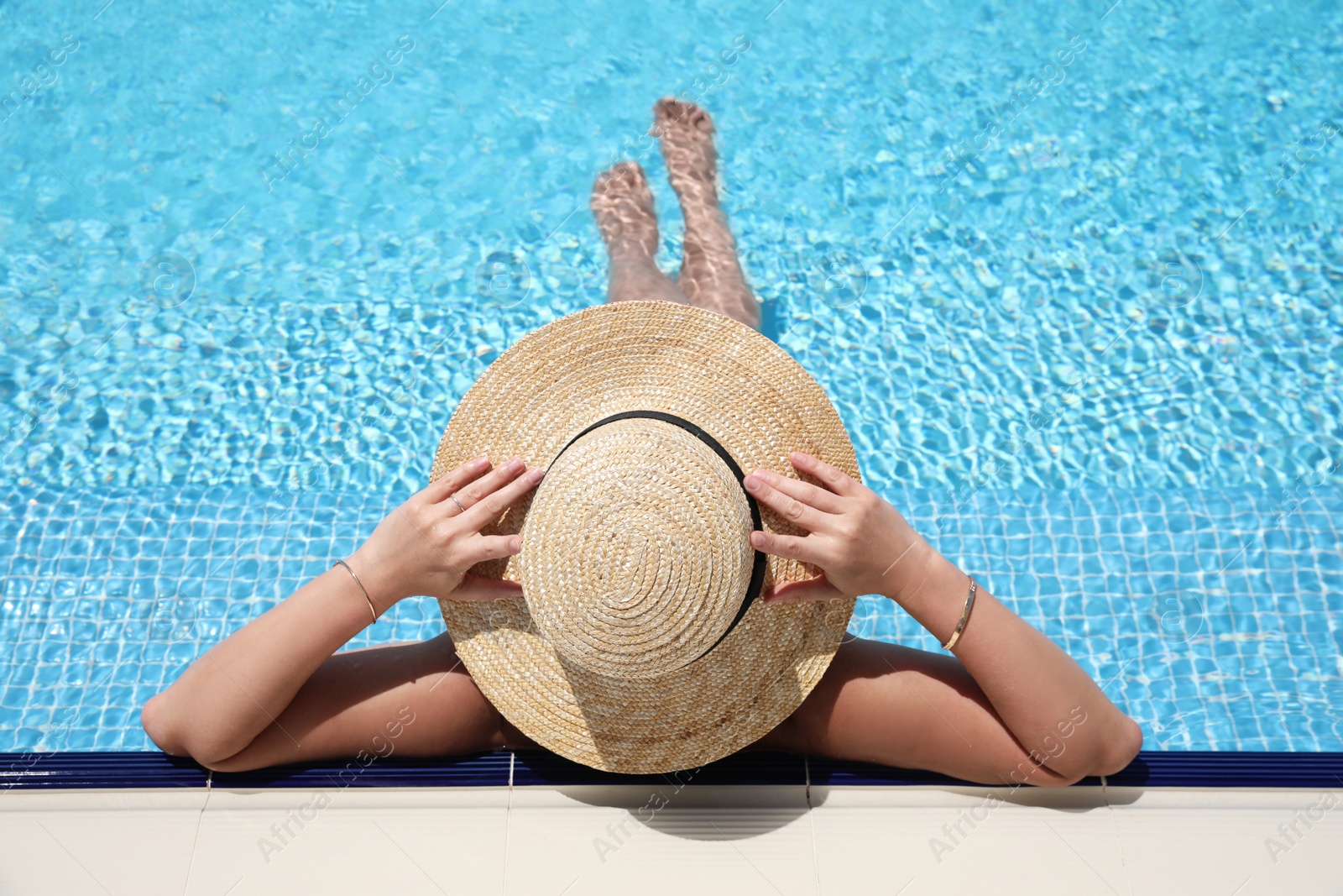 Photo of Woman with straw hat resting in outdoor swimming pool on sunny day, above view